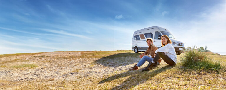 Kastenwagen mit sitzendem Paar auf Wiese. Sonniges Bild am Strand.